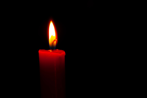 A red candle with a flame on a black background. Copy space. Horizontal snapshot. The concept of memory, sorrow, hope, rip., tragedy, emergency.