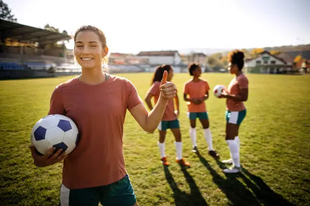 Portrait of a young beautiful woman who plays football, in the background you can see other players