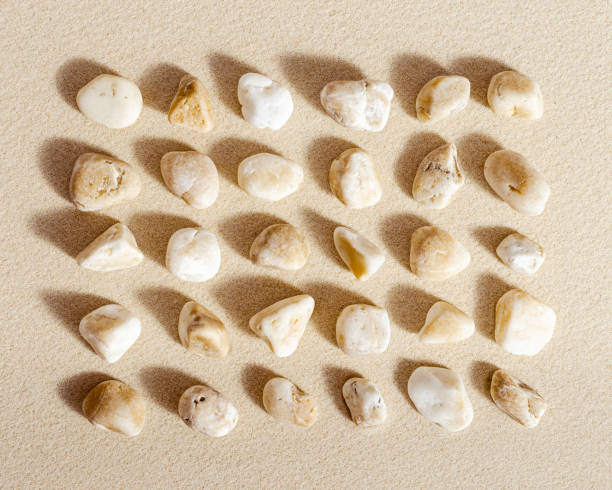 istock Pattern with white pebble sea stones on fine sand. Square composition from natural stone neutral beige color, monochrome tones. Spa minimal background 1350464901