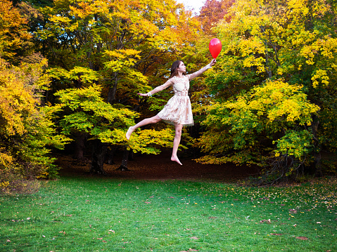 Happy young brunette woman holding a red balloon and flying, with an autumn scenery in the background. 

Location, S. Antonio Woods, Pescocostanzo (AQ); Maiella National Park, Abruzzo, Italy, Europe.