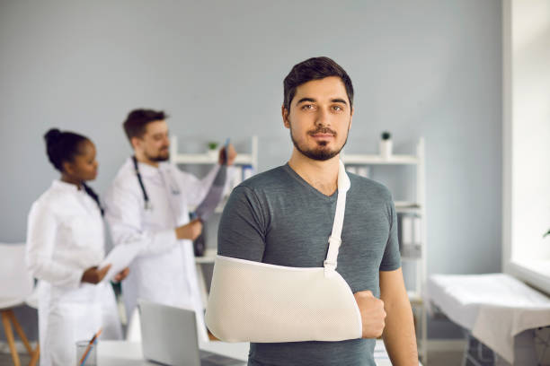 portrait of caucasian man with bandage on broken hand standing in hospital ward - arm sling imagens e fotografias de stock