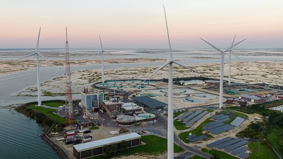 Sustainable energy is used in environmental conservancy. A wastewater treatment plant powered by wind turbines and solar panels near Atlantic City in New Jersey, USA. Aerial elevated view at the sunset.