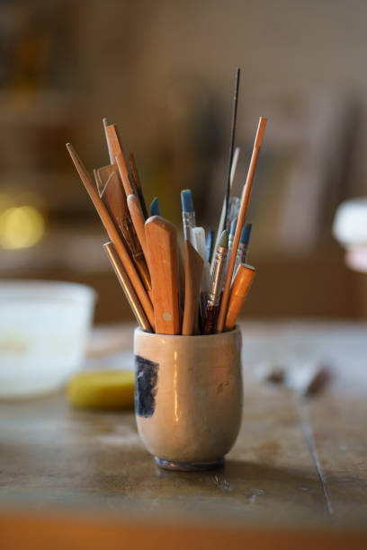 istock Paintbrush with tools for pottery shaping in bowl on table. Ceramics equipment in creative art space 1350473024