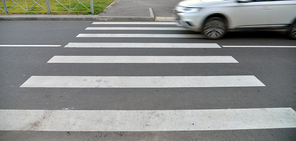 White Car is driving past a pedestrian crossing. Car blurred in motion.