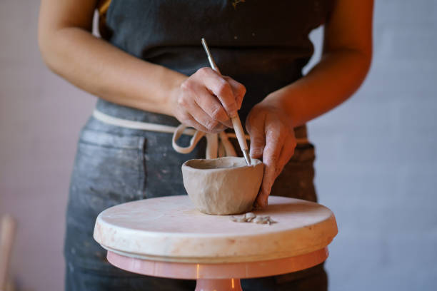 Woman potter in apron shape vase of wet clay on pottery wheel. Ceramist artist female work in studio Cropped image of potter in apron shaping vase of raw clay use professional tools and pottery wheel. Ceramist artist female work in studio. Craft ceramics production small business and entrepreneurship pottery making stock pictures, royalty-free photos & images