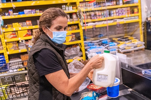 Caucasian Mature women packing her groceries at the cashier zone of a supermarket wearing a protective face mask