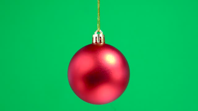 Red matte christmas toy ball is spinning on a green plain background