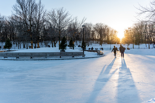 People skating on ice rink in Mount Royal park, Montreal, during a sunset of winter.