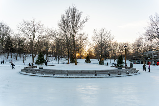People skating on ice rink in Mount Royal park, Montreal, during a sunset of winter.