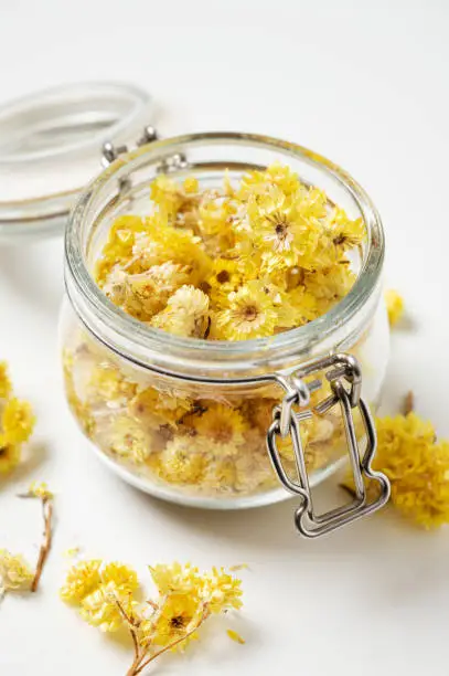 Photo of Helichrysum italicum. Yellow dried herb  flowers in a jar close-up on a white background