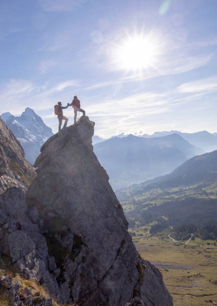 日当たりの良い岩の頂点に登山家ハイファイブ - pinnacle ストックフォトと画像