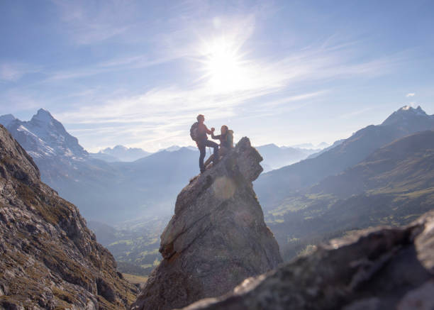Silhouette of young woman backpacker and her small fluffy cute pug enjoying the view of big mountain during cloudy day in Swiss Alps - feeling freedom and awe