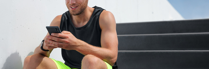 Man using phone connected to fitness smartwatch health monitoring of body and sports data from exercising. Active healthy people lifestyle banner panoramic crop of smartphone and smart watch.