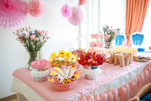 Birthday cake on a table against a wall with decoration flags and balloons. Party table with daisies, cupcake liner topiary and garlands. Baby shower