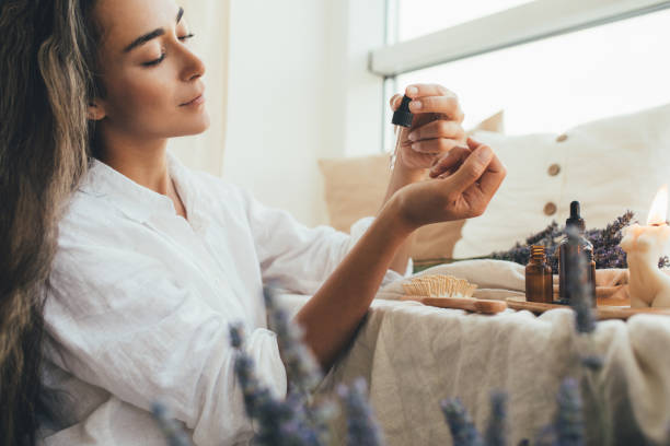 mujer joven aplicando aceite esencial orgánico natural en el cabello y la piel. spa casero y rituales de belleza. - perfume bottle scented cosmetics fotografías e imágenes de stock