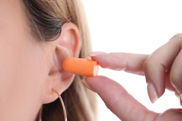 Woman inserts soft orange earplugs into ear closeup Woman inserts soft orange earplugs into ear. Selection of silicone earplugs concept stopper stock pictures, royalty-free photos & images