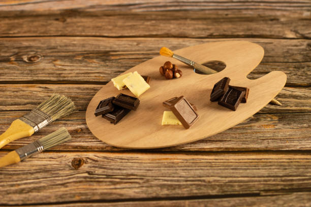 Assorted chocolates are set on an artistic palette against a warm wooden background. Concept - drawing with chocolate, picture for a cafe, conceptual photo