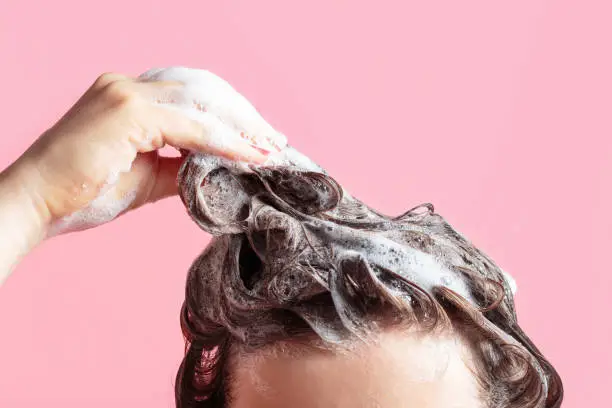 A girl washes her hair with shampoo on a pink background, front view.