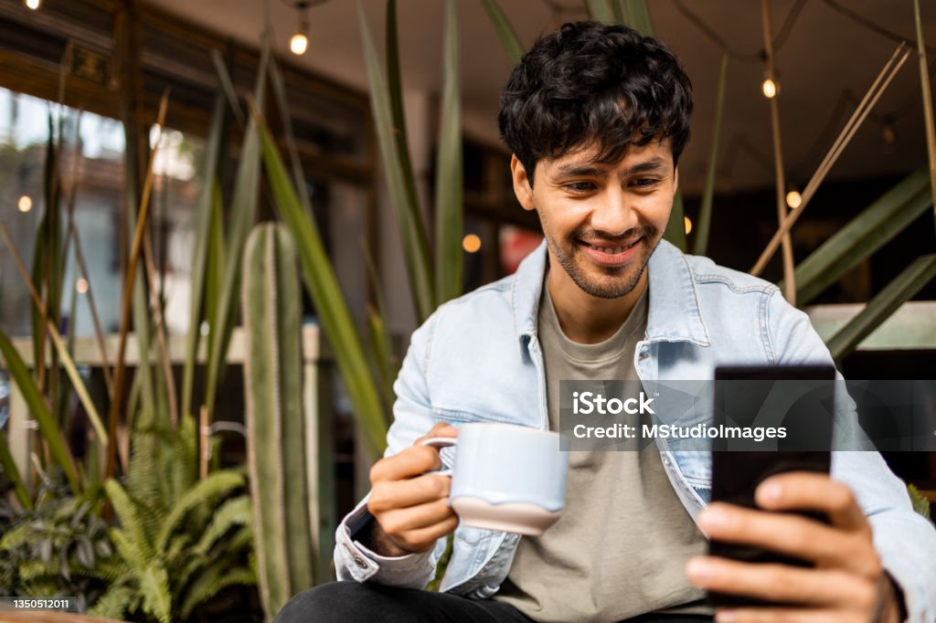 Having a morning coffee. Young Latin man relaxing with the mobile phone while having a morning coffee Mobile Phone Stock Photo