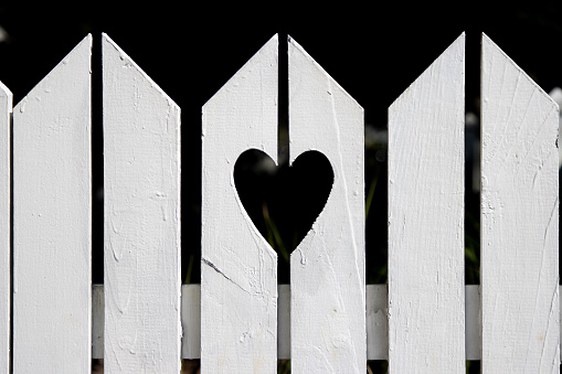 A fence outside the yard of a house in the suburbs with a love heart shape cut out.