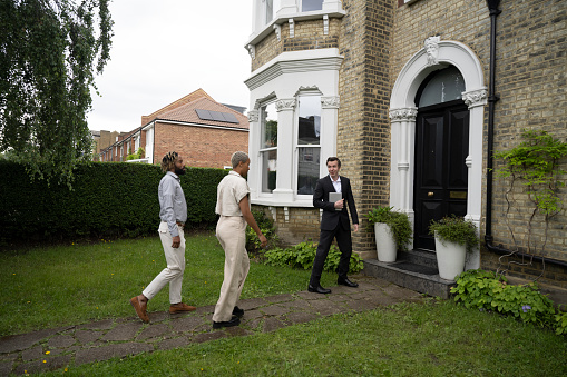 Full length view of mid adult Black couple following estate agent up path to front door of restored 1890 Victorian home.