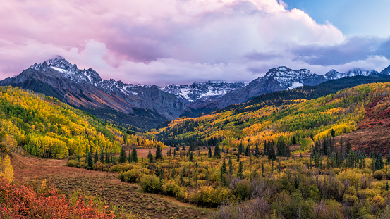 A colorful valley with the East Fork of Dallas Creek and WIllis Swamp with dramatic Fall colors below Mount Sneffels and moody sunset clouds in the San Juans Mountains of Southwest Colorado.