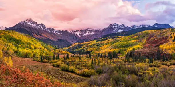 A colorful valley with the East Fork of Dallas Creek and WIllis Swamp with dramatic Fall colors below Mount Sneffels and moody sunset clouds in the San Juans Mountains of Southwest Colorado.
