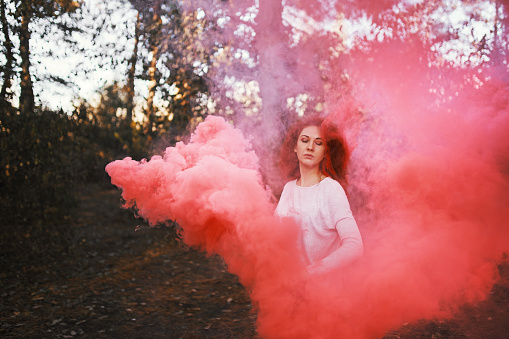 Smoke screen in the woods. Woman with smoke. Beautiful woman with pink smoke behind her in the forest