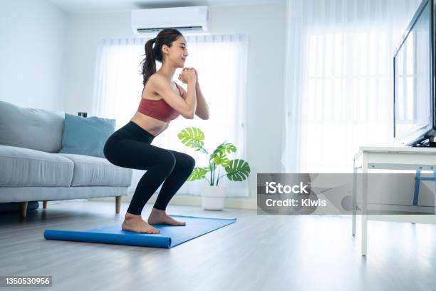 Asian Beautiful Young Woman Stay Home Doing Aerobic Exercise At Home Attractive Girl Doing Lockdown Activity Workout By Squatting Follow Instructions Video From Online Trainer For Health In House Stock Photo - Download Image Now