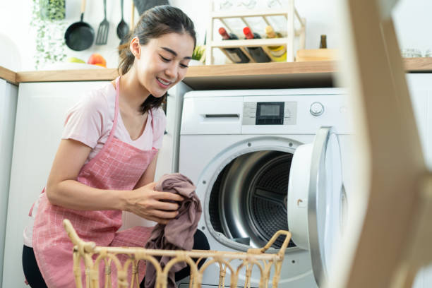 Asian beautiful woman put dirty clothes to washing machine in house. Attractive girl wear apron sit on floor, feel happy to loads laundry in washer appliance at home. Domestic-House keeping concept. Asian beautiful woman put dirty clothes to washing machine in house. Attractive girl wear apron sit on floor, feel happy to loads laundry in washer appliance at home. Domestic-House keeping concept. asian laundry stock pictures, royalty-free photos & images