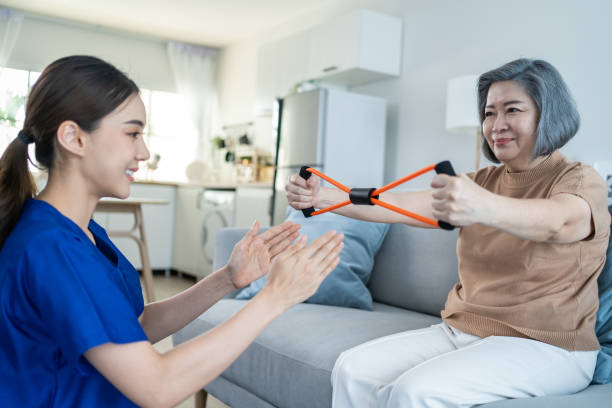 istock Asian Disabled old woman doing physiotherapist with support from nurse. Senior elder handicapped female sit on sofa in living room use resistance stretch band exercise for patient in home nursing care 1350531003