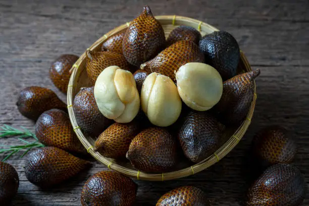 Photo of Fresh Waive fruit in Bamboo basket on wooden table, Fresh Salak or Snake Fruit tropical fruit on a wooden table.