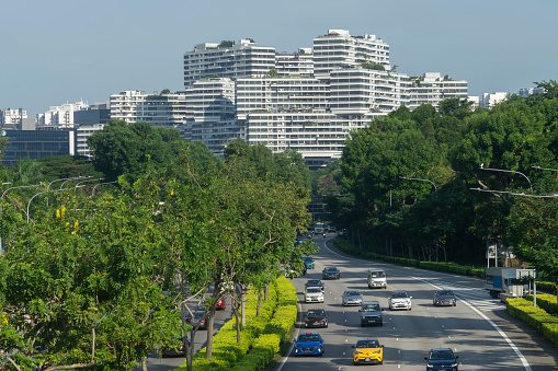 Singapore, Singapore - September 20, 2021: Vehicles on a motorway before The Interlace, an apartment complex resembling shipping containers stacked on top of each other.
