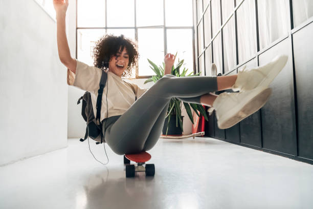 Playful young multiracial woman sliding down a corridor sitting on skateboard having fun Playful young multiracial woman sliding down a corridor sitting on skateboard having fun. Lifestyle concept. playing alone stock pictures, royalty-free photos & images