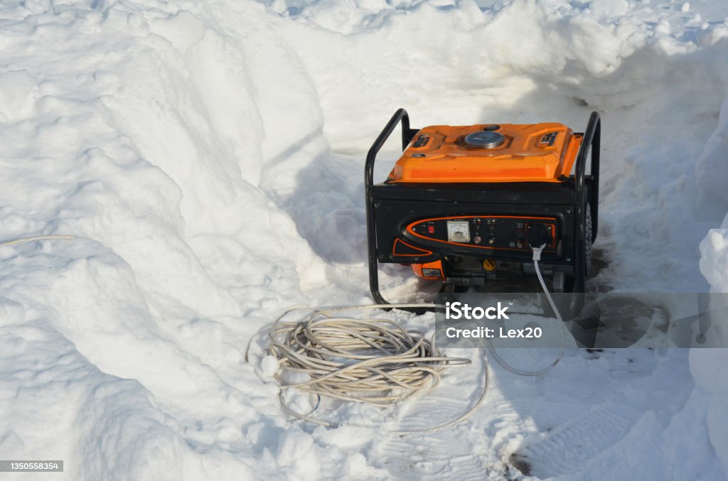 A portable generator, backup power generator around snow after severe winter weather, blizzard and snow storm. Using a mobile generator to provide power after snowy weather. Generator Stock Photo