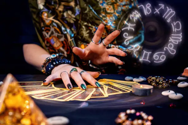 A witch spread out her tarot cards on the table. Hands close-up. The zodiac circle in the upper right corner. The concept of divination and astrology.
