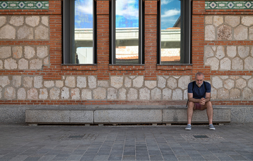 Adult man sitting on bench in front of brick building. Shot in Matatero, Madrid, Spain.