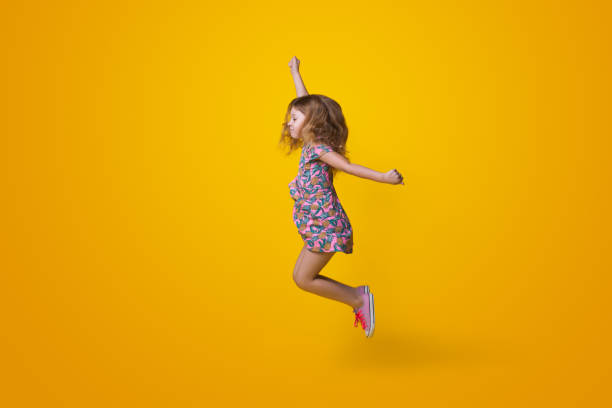 istock Small ginger girl is jumping on a yellow studio wall imitating super hero 1350571004