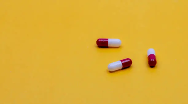 Red-white capsule pills on yellow background. Pharmacy web banner. Prescription drug. Pharmaceutical industry. Online pharmacy. Pharmacology. Health budget and health insurance. New drug research.