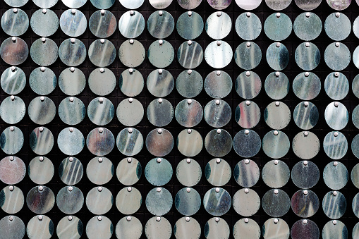 A defocused shot of repeating metallic shiny circles. A multitude of round-shaped objects fluttering in the wind.