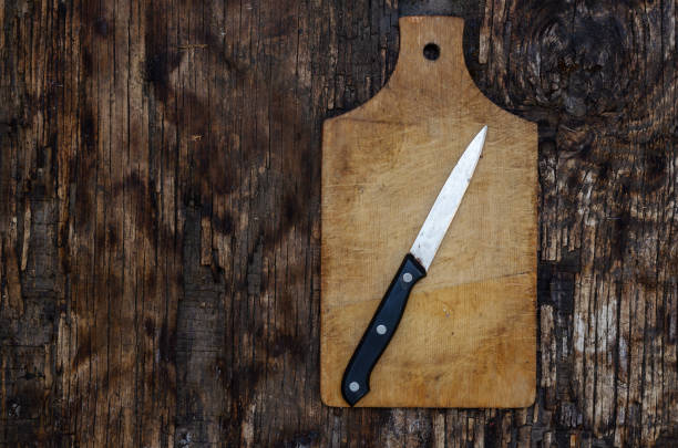 Kitchen knife and cutting board on cracked wooden background. Top view. Selective focus.