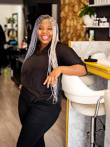 Portrait of a successful beautician with box braids standing in her beauty salon looking at camera and smiling