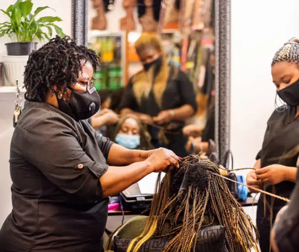 Photo of Hairstylists braiding and extending a client's hair in salon