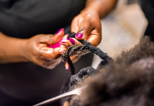 Close-up of a hairstylist hands using tools while braiding and extending customer's hair in her beauty salon