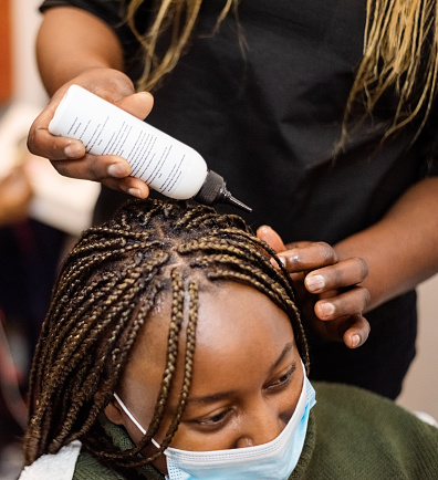 Woman wearing face mask with braided hair in salon getting her hair groomed with oil