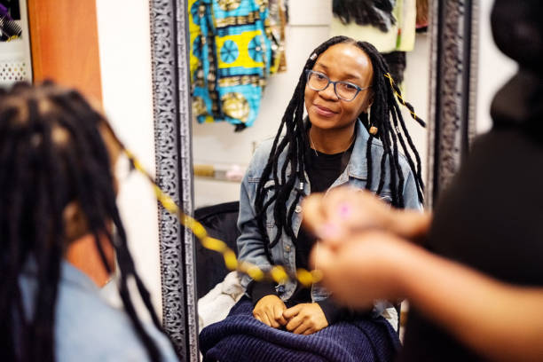 African woman getting her hair braided in salon Mirror reflection of a female client getting her hair braided with thread at beauty salon hair threading stock pictures, royalty-free photos & images