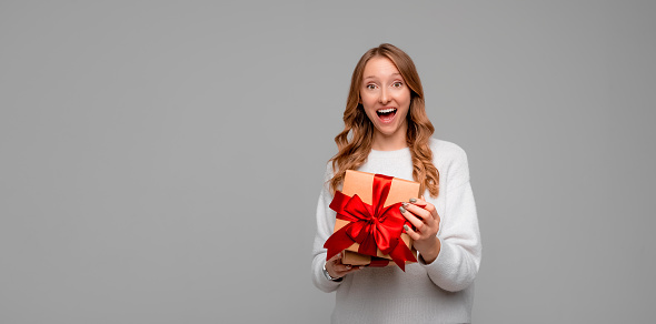 Beautiful young woman in white sweater holding in hands unboxed present and looking at camera with smiling broadly. Holidays, celebration and lifestyle concept. Mock up copy space