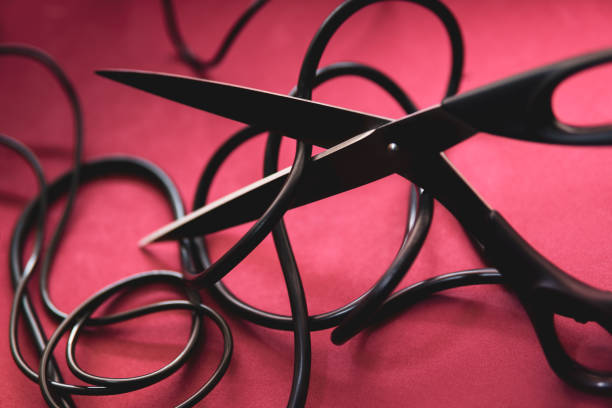 Scissors threaten to cut the black electric cable on a red background