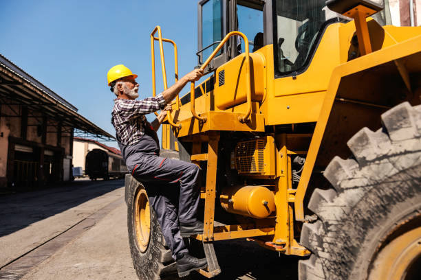 starszy pracownik przemysłu ciężkiego wspina się na buldożer i przygotowuje się do jazdy nim. kierowca wspinający się na buldożer. - construction equipment large construction crane zdjęcia i obrazy z banku zdjęć