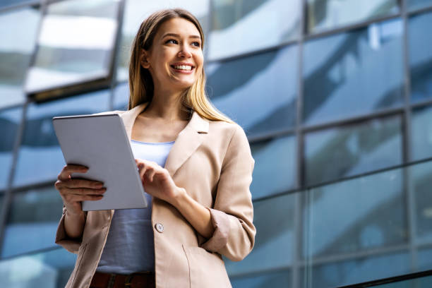Successful businesswoman using a digital tablet while standing in front of business building. stock photo